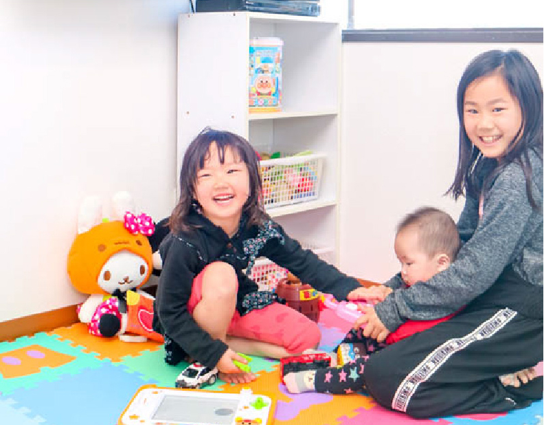 室内の遊び場で笑顔の女の子と他の子どもが玩具で遊ぶ様子