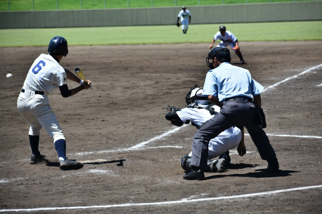 野球の試合中、打者がバットを構え捕手と審判が見守るスポーツ障害治療のイメージ。