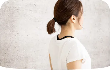 白いTシャツを着た女性が壁際に立つ、後ろ姿の写真